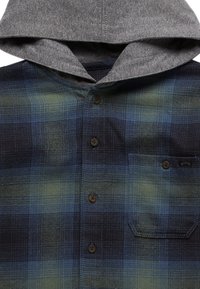 Camisa de franela a cuadros con capucha gris, tonos azules y verdes, cierre de botones y un solo bolsillo en el pecho con una etiqueta.