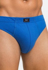 Slip in cotone blu con fascia elastica che presenta un'etichetta nera. Texture liscia, design aderente, con cuciture visibili lungo le cuciture.