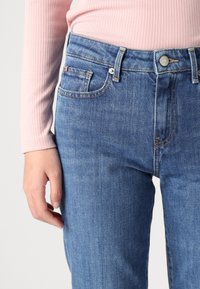 Ljusblå denimjeans med en figurnära passform, midja i normalhöjd och kontrasterande sömmar. Framfickor är synliga, i kombination med en rosa ribbad topp.