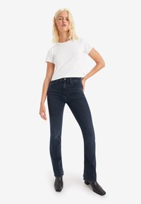 Vit kortärmad t-shirt kombinerad med mörka denim raka jeans. Modell som bär svarta ankelskor, med ljust blont hår stylat rakt.