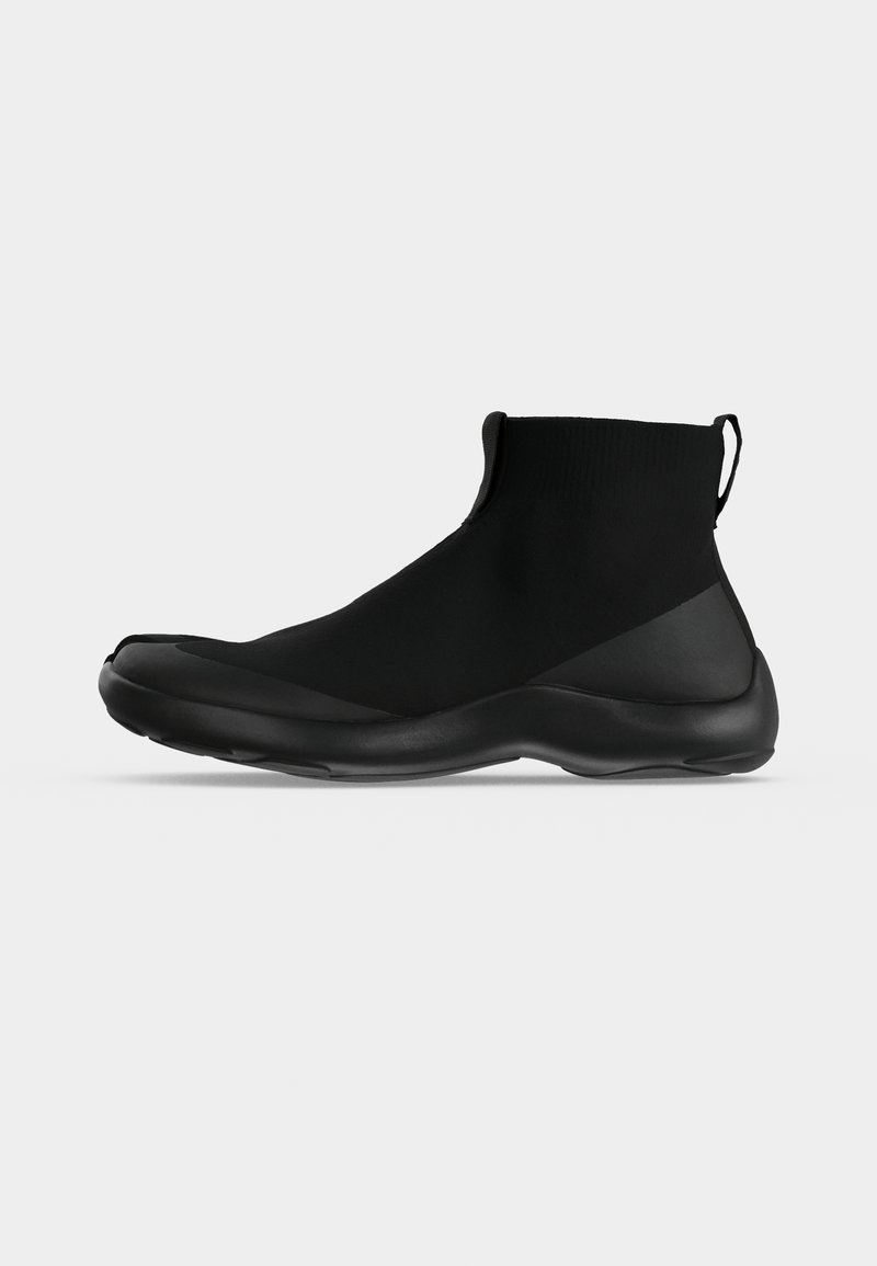 Chaussure de sport noire montante à la cheville avec une tige type chaussette, une languette à l’arrière et une semelle épaisse et rembourrée, présentée de profil sur fond blanc.