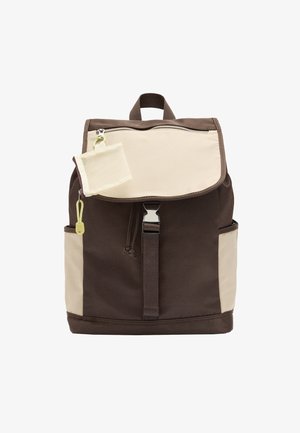 Ciemnobrązowy i beżowy plecak z przednią klapką, metalową klamrą, bocznymi kieszeniami, górnym uchwytem oraz małą beżową saszetką na zamek.