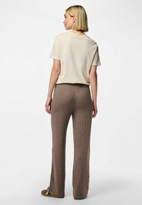 Haut court beige clair à manches courtes associé à un pantalon marron côtelé. Le pantalon présente des rayures verticales, tandis que le haut a un col rond standard.