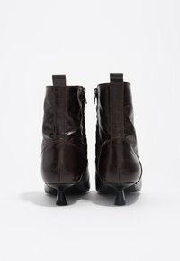 Botas de cuero marrón hasta el tobillo con cremalleras, detalles de costura y un tacón estrecho. La parte posterior muestra una textura suave y un diseño minimalista.