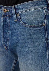Blue denim jeans featuring a classic five-pocket design, contrast stitching, and a zipper fly with a metal button closure.
