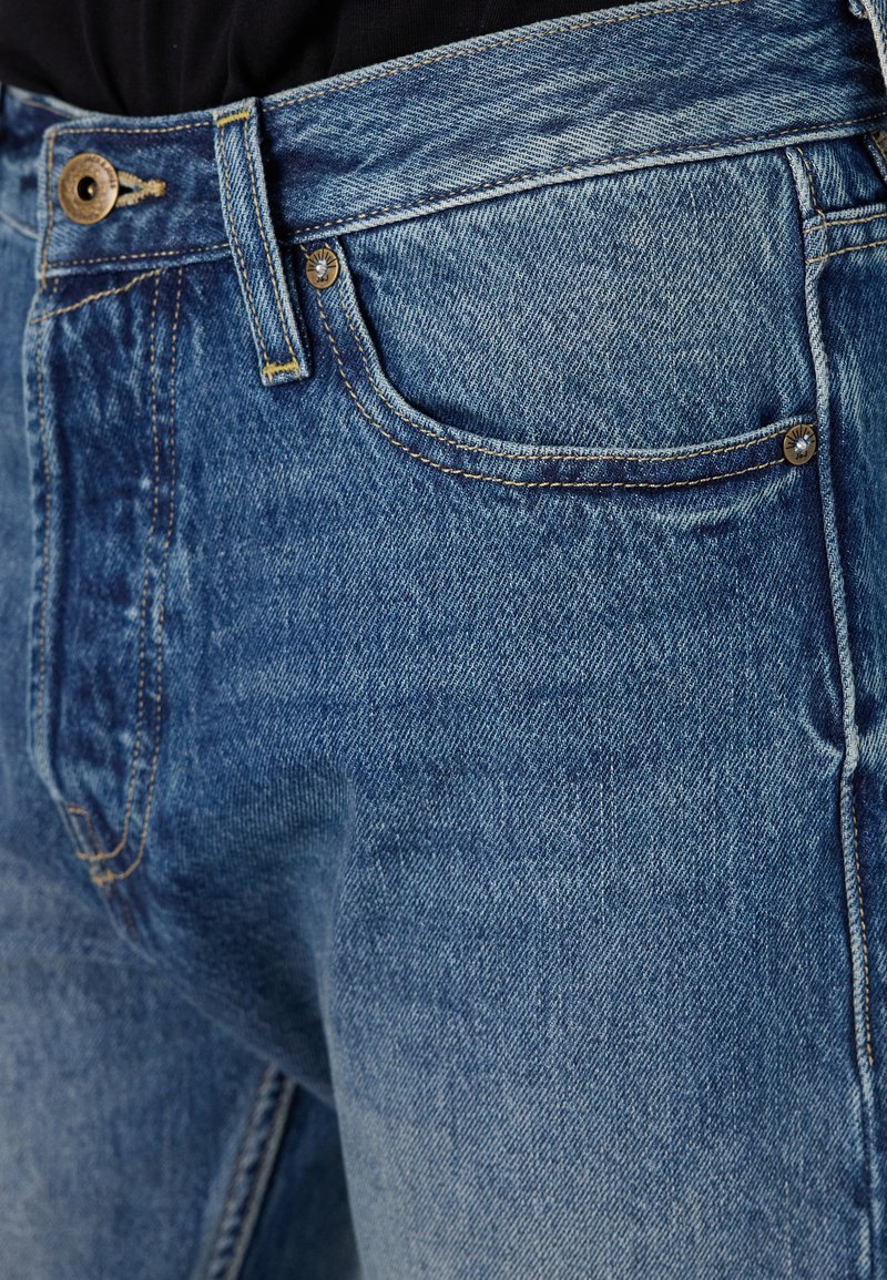 Jeans de mezclilla azul con un diseño clásico de cinco bolsillos, costuras de contraste y un cierre de cremallera con botón de metal.