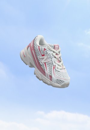 Chaussure de course New Balance blanche et rose avec un design en mesh, flottant sur un fond de ciel bleu clair.