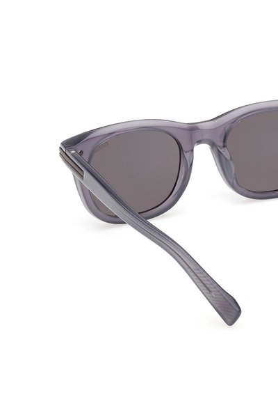 Harmaansävyiset aurinkolasit, joissa läpinäkyvä harmaa kehys. Kissansilmämuotoiset, sileä pinta ja pystysuorat uurteet sankojen kohdalla.