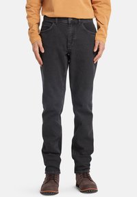 Donkergrijze jeans met een rechte pasvorm, voorzien van voorzakken en subtiele stiksels. Draag een lichtoranje langemouwenshirt en bruine laarzen.