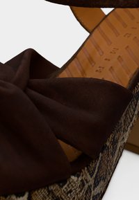 Καφέ πλατφόρμες σανδάλια με υφαντή βάση με υφή και σχέδιο και μεγάλο καφέ υφασμάτινο φιόγκο στην κορυφή. Διαθέτουν ομαλή εσωτερική επένδυση.