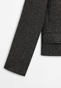 Grijze blazer met een visgraatpatroon en een gestructureerd ontwerp, voorzien van een enkele zak en een getailleerde pasvorm. Zacht, textuurgegeven stof.