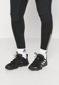 Scarpe sportive nere con dettagli rosa, tomaia texturizzata, strisce bianche e suole nere. Abbinati a calzini bianchi e leggings neri con zip.