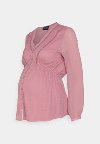 Blouse de maternité en tissu rose doux à texture à pois, avec encolure en V, fermeture à boutons, froncée sous la poitrine, et manches longues.