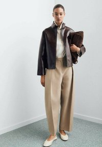 Brown leather jacket with a collar, paired with beige wide-leg trousers. Holding a brown bag, beige slip-on shoes complete the look.