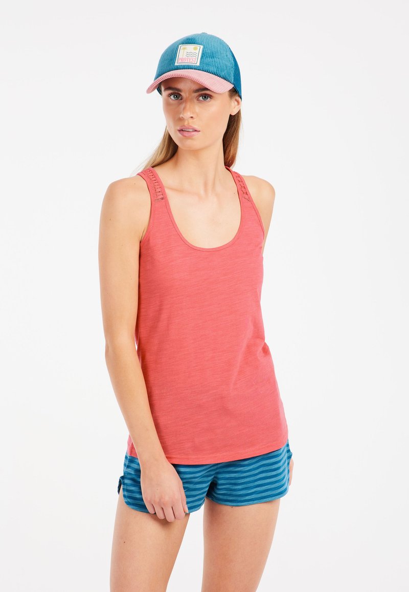 Korallfarbenes Tanktop mit strukturierten Schulterträgern, kombiniert mit blauen gestreiften Shorts. Die Kappe hat eine blaue Cordfront und einen pinken Schirm mit Logo.