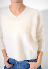 Maglione a V color crema realizzato in materiale morbido e peloso, con maniche lunghe e polsini a costine, abbinato a jeans in denim blu a vita alta.