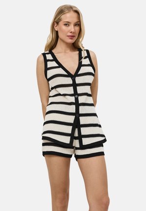 Vrouw draagt een mouwloze V-hals gebreide top met knopen en bijpassende korte broek met zwarte en witte horizontale strepen.