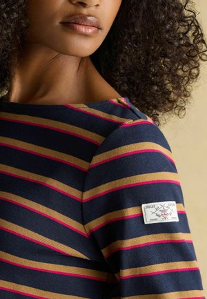 Navy striped top featuring horizontal gold and pink lines, crew neck design, and a logo patch on the left sleeve. Soft, textured fabric.