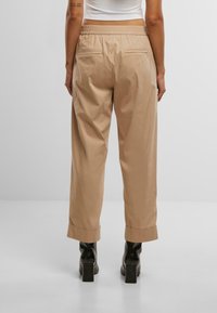 Pantaloni in cotone beige con vita elastica, taglio dritto, orli arrotolati e due tasche posteriori. Indossati con stivaletti neri con tacco a blocco.
