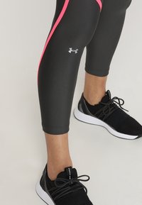 Des leggings de sport noirs présentent des rayures latérales roses et un design ajusté. Associés à des baskets noires, mettant en valeur une tige en maille et une semelle blanche.