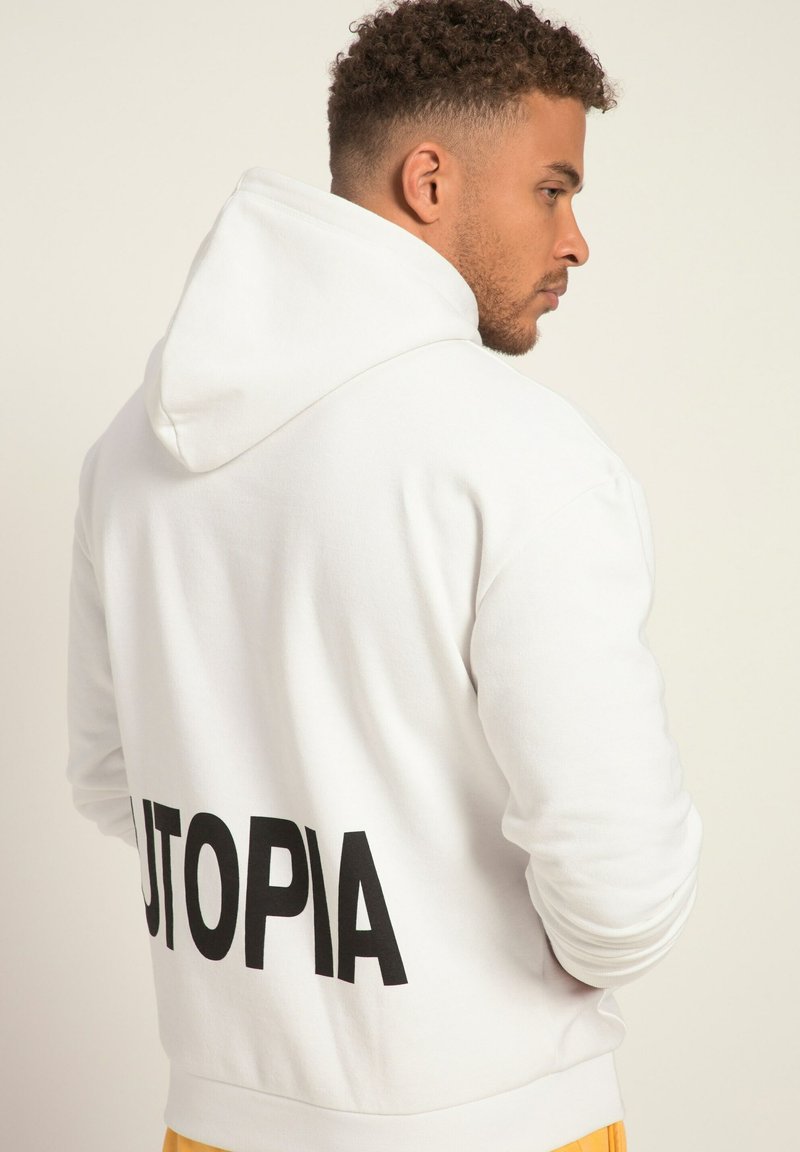 Vit hoodie gjord av mjukt tyg, med en stor svart "UTOPIA"-tryck bak, standardhuva och ribbade muddar.