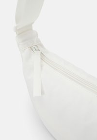Bílé látkové crossbody taška se zipovou kapsou a texturovaným popruhem. Disponuje hladkým povrchem a minimalistickým designem.
