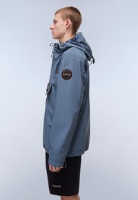 Lichtblauwe, waterdichte jas met een capuchon, voorzien van een logopatch op de linkermouw en een voorzak. Gladde textuur, casual pasvorm.