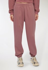 Joggers attillati a vita alta in mauve, tessuto testurizzato con polsini e vita elasticizzati, abbinati a sneakers beige con accenti grigi.