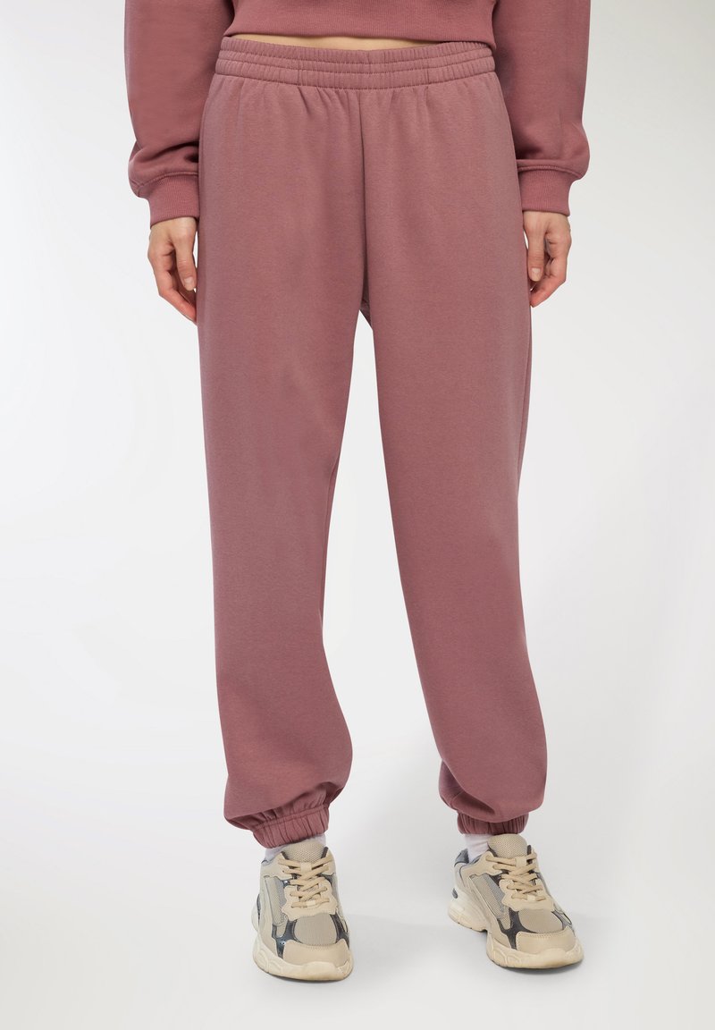 Joggers attillati a vita alta in mauve, tessuto testurizzato con polsini e vita elasticizzati, abbinati a sneakers beige con accenti grigi.