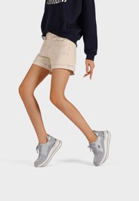 Scarpe sportive grigie con una tomaia testurizzata, accenti a contrasto e una suola imbottita, indossate con pantaloni corti beige e una felpa blu navy.