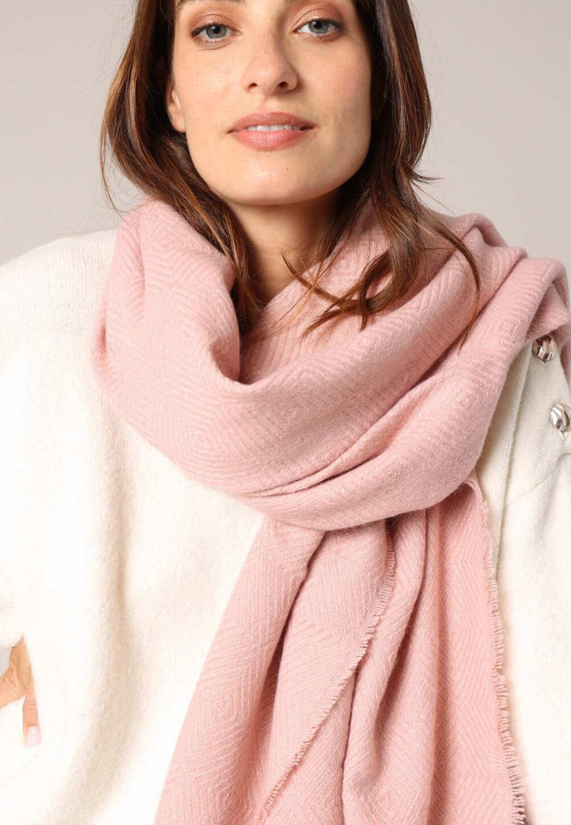 Écharpe rose clair avec un motif en chevron, fabriquée dans un matériau doux, drapée autour du cou, avec des bords effilochés, associée à un top blanc.