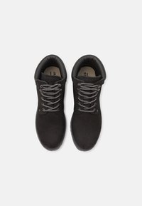 Zapatos de ante negro con punta redonda, cordones grises y cuello acolchado. Suela de goma texturizada. Diseño minimalista con un enfoque en la comodidad.