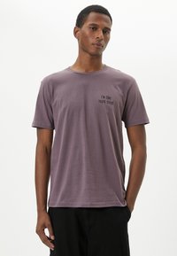 Lila bomull t-shirt med korta ärmar och rundad halsringning, med svart text som säger "Jag är typ 104% trött" på vänster bröst.