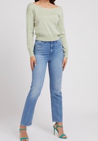 Jasnozielony sweter z odsłoniętymi ramionami, zestawiony z niebieskimi, prostymi jeansami oraz zielonymi, paskowanymi szpilkami. Miękka faktura i casualowa sylwetka.