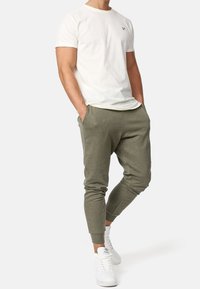 Witte katoenen T-shirt met ronde hals en logo op de linkerborst, gecombineerd met olijfgroene tapered joggers en witte sneakers.