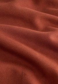 Tissu doux de couleur rouille avec une texture fine en maille visible et des plis légers créant une surface lisse et ondulée.