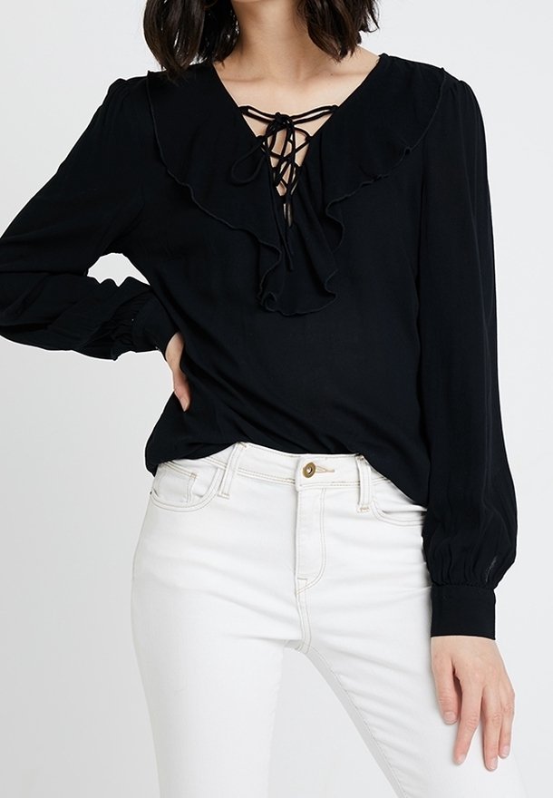 Blusa nera a maniche lunghe con scollatura arricciata e dettaglio con lacci, abbinata a jeans bianchi. Tessuto morbido e maniche gather.