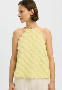 Žlutý halter top vyrobený z texturované látky s diagonálními třásněmi. Lehký, s úzkým výstřihem a vrstevnatým vzhledem.