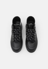 Par de zapatillas altas de cuero negro con cordones a rayas negras y blancas, suelas acanaladas y la marca "KARL" en la lengüeta.