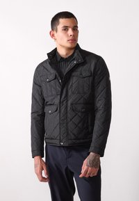 Black quilted jacket with a high collar, four front pockets, and snap closures. Textured fabric and tailored fit for a modern look.