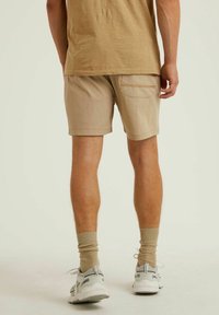 Pantalones cortos beige con un bolsillo trasero, hechos de tela ligera. Llevados con calcetines beige hasta el tobillo y zapatillas deportivas grises.
