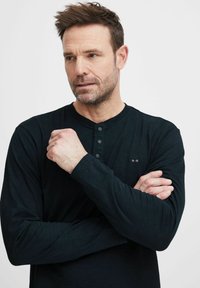 Must mustrekiv allääne T-särk viie nupuga, peene logo detailiga, ümmarguse kaelusega ja tekstureeritud kangaga. Lihtne, keha lähedal disain.