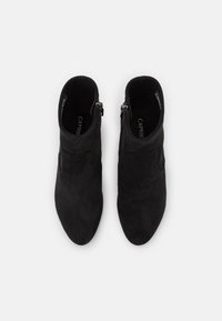 Czarne zamszowe botki za kostkę o eleganckim, stożkowym kształcie palców oraz zapięciem na zamek po bokach. Miękka tekstura i minimalistyczna estetyka.