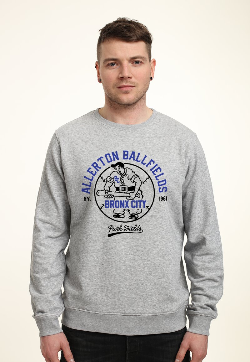 Sweat-shirt gris à col rond ; présente un graphique imprimé d'un joueur de baseball, avec le texte "Allerton Ballfields Bronx City 1961" en bleu et noir.