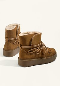 Rjave semenski gležnjarji s mehkim umetnim krznom, imajo debel podplat in vezalke za varen oprijem. Teksturirana površina in zasnova zaobljenega nosa.