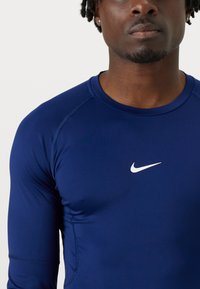 Marineblaues, langärmliges Sportshirt aus dehnbarem Material, mit einem weißen Nike-Logo auf der Brust und Kontrastnähten.