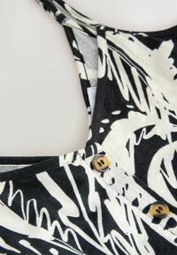 Schwarzes und weißes gemustertes Tanktop mit U-Ausschnitt, dünnen Trägern und zwei runden braunen Knöpfen am Ausschnitt. Weiche Stofftextur.