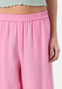Pantaloni di colore rosa chiaro, morbidi e comodi, con una cintura elastica e tessuto texturizzato. Il design presenta una gamba ampia per comfort e traspirabilità.