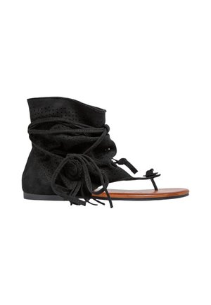 Sandale plate en daim noir avec attache cheville, tissu perforé, fermeture nouée et boucle pour les orteils sur semelle marron sur fond blanc.