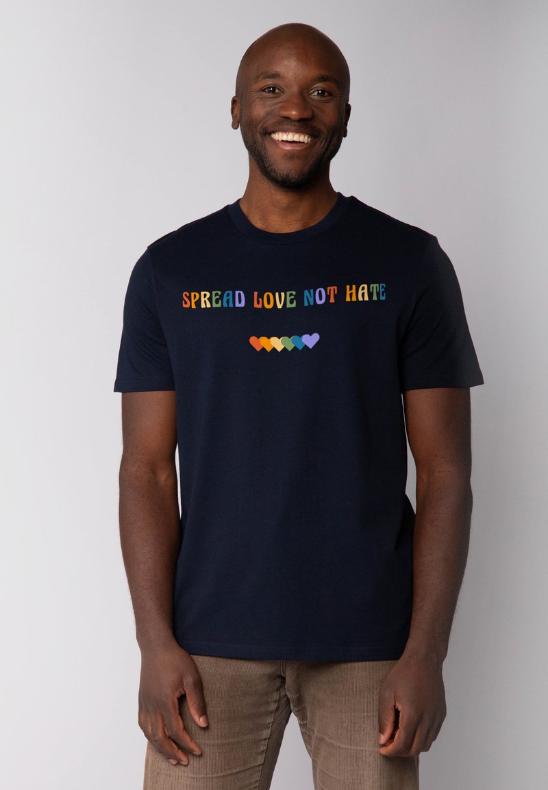 T-shirt en coton marine à manches courtes, arborant un texte multicolore "RÉPANDRE DE L'AMOUR PAS DE HAINE" et des motifs de cœurs colorés en dessous.